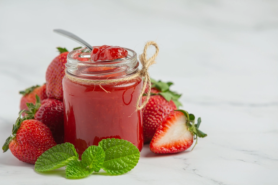 Fresh strawberry puree in a glass jar with strawberries around it